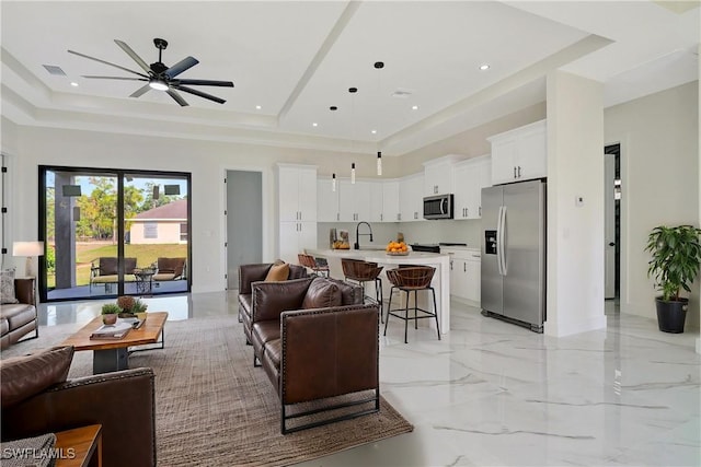 living room featuring ceiling fan, sink, and a tray ceiling