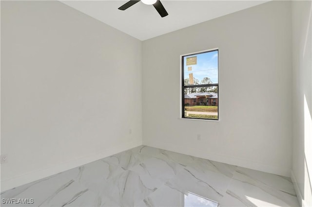 empty room featuring marble finish floor, a ceiling fan, and baseboards