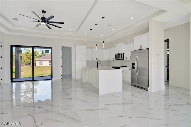 kitchen with marble finish floor, stainless steel appliances, a tray ceiling, and an island with sink