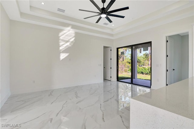 spare room with marble finish floor, a raised ceiling, a ceiling fan, and baseboards