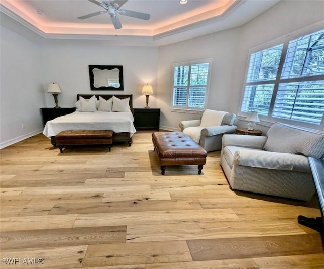 bedroom featuring ceiling fan, light hardwood / wood-style floors, and a tray ceiling