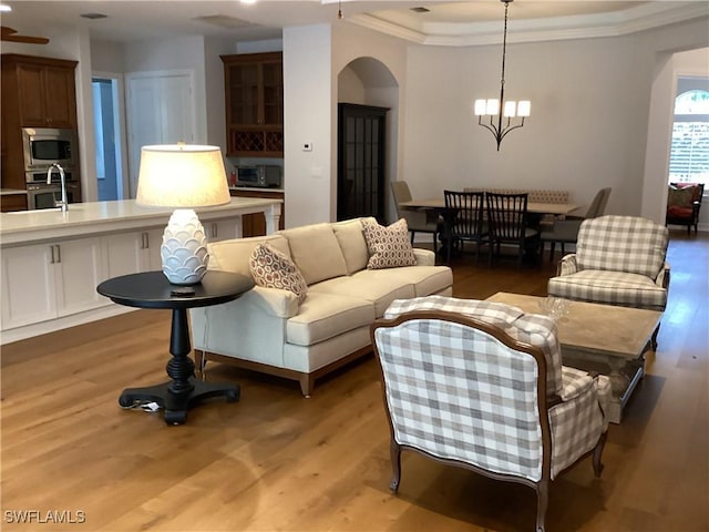 living room featuring ornamental molding, a chandelier, a raised ceiling, and light hardwood / wood-style flooring