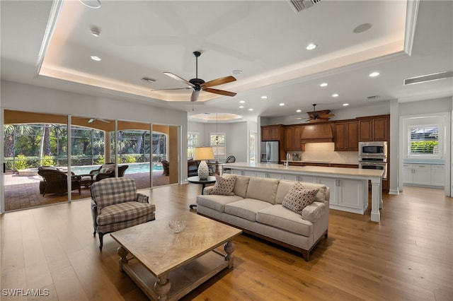 living room featuring ceiling fan, a healthy amount of sunlight, a raised ceiling, and light hardwood / wood-style flooring