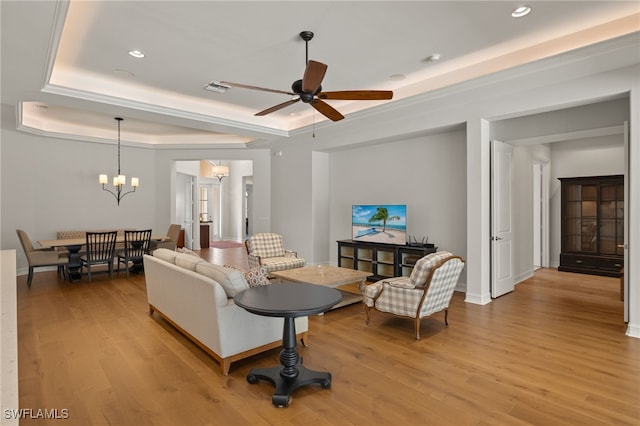 living room with ceiling fan with notable chandelier, a tray ceiling, and light hardwood / wood-style floors