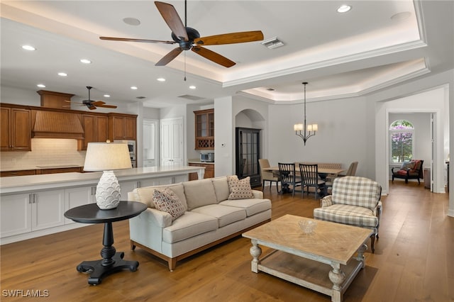 living room with a tray ceiling, ceiling fan with notable chandelier, and light wood-type flooring