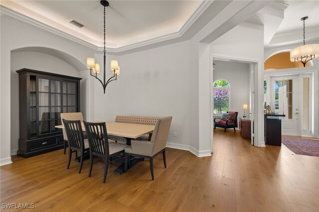 dining room featuring crown molding, a tray ceiling, light hardwood / wood-style floors, and a notable chandelier