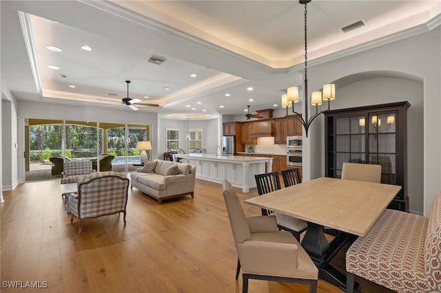 dining space with a tray ceiling, ceiling fan with notable chandelier, and light hardwood / wood-style floors