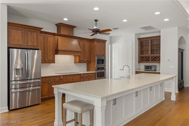 kitchen featuring appliances with stainless steel finishes, sink, a kitchen bar, a kitchen island with sink, and light wood-type flooring