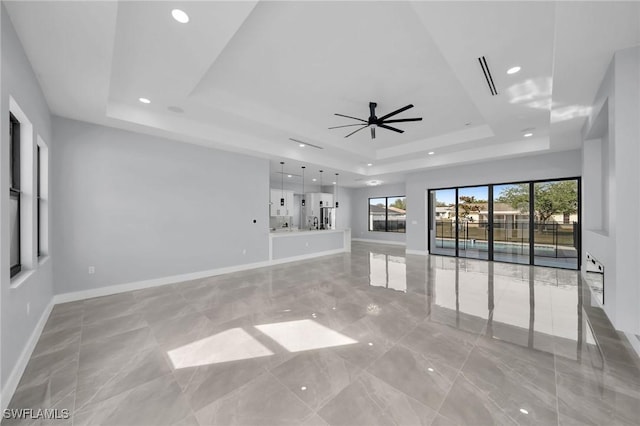 unfurnished living room with ceiling fan and a tray ceiling