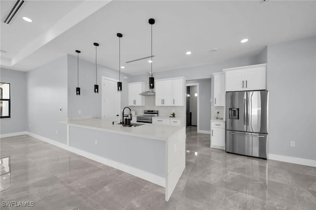 kitchen with appliances with stainless steel finishes, wall chimney range hood, pendant lighting, white cabinets, and sink