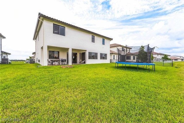 back of house featuring a trampoline, a yard, and central AC