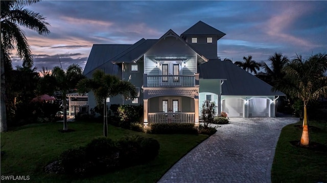 view of front facade with french doors, a balcony, a garage, and a lawn