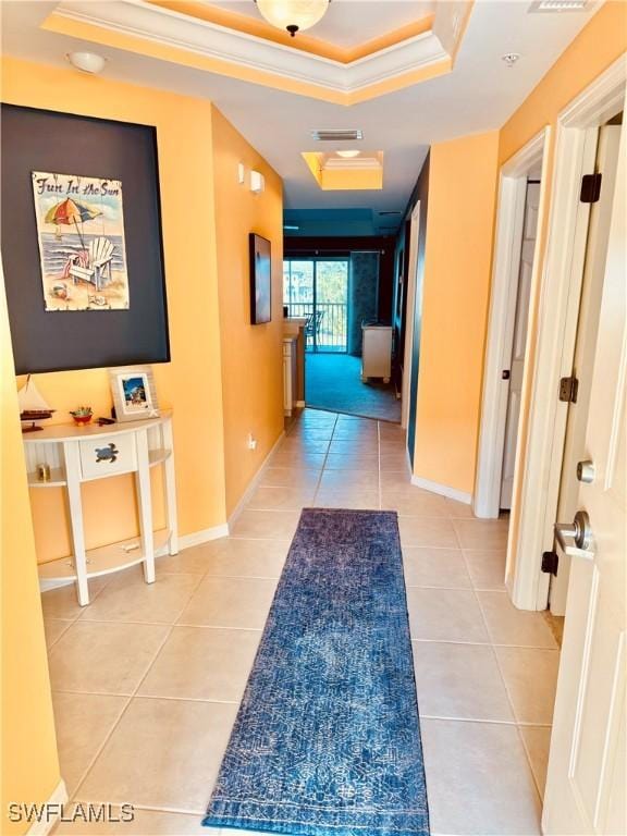 hall featuring light tile patterned floors, a tray ceiling, and crown molding