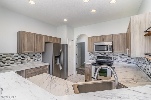 kitchen featuring a textured ceiling, stainless steel appliances, tasteful backsplash, sink, and light stone counters