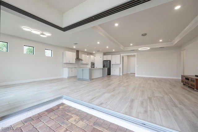 kitchen featuring a raised ceiling, light countertops, open floor plan, white cabinetry, and black fridge