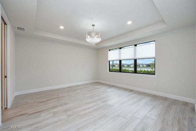 unfurnished room with baseboards, a raised ceiling, light wood-style flooring, and an inviting chandelier