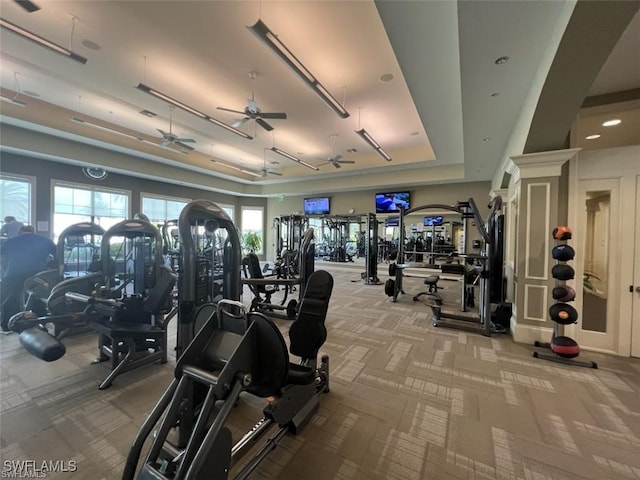 gym featuring a raised ceiling and ceiling fan