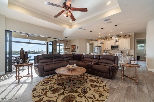 living room with crown molding, a water view, light hardwood / wood-style floors, and a tray ceiling