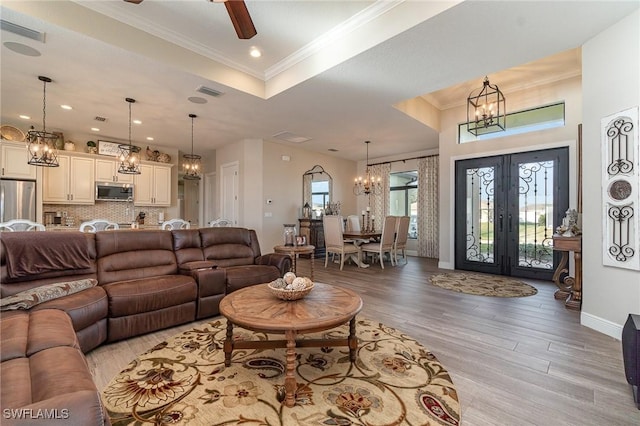 living area with french doors, baseboards, visible vents, light wood-style floors, and crown molding