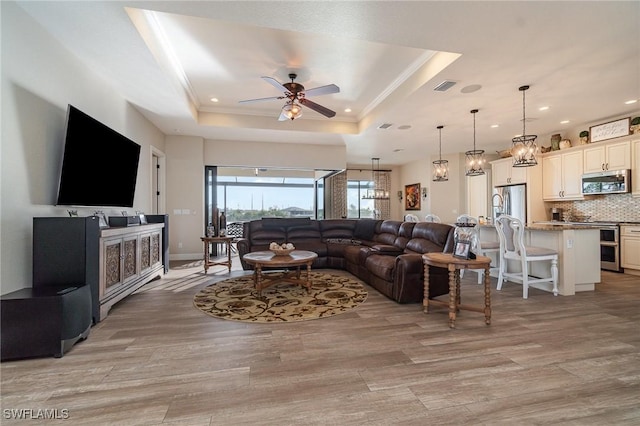 living room featuring a raised ceiling, ornamental molding, ceiling fan, and light hardwood / wood-style floors