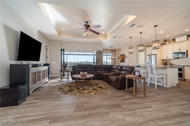 living room featuring visible vents, light wood-style flooring, a tray ceiling, and ceiling fan