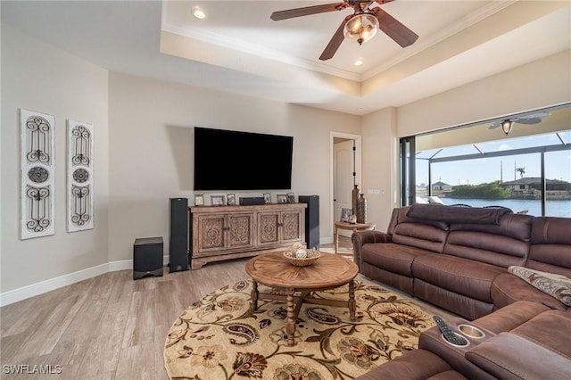 living room with light wood finished floors, a raised ceiling, baseboards, a ceiling fan, and ornamental molding