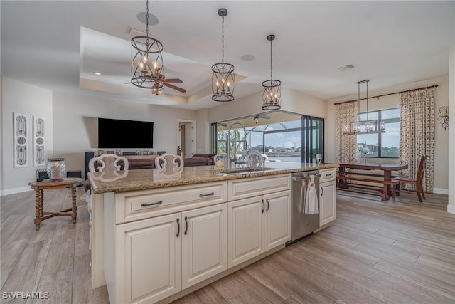 kitchen featuring light hardwood / wood-style flooring, dishwasher, a kitchen island with sink, a tray ceiling, and decorative light fixtures