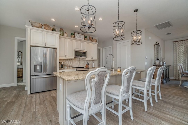 kitchen featuring light stone countertops, appliances with stainless steel finishes, a center island with sink, and decorative light fixtures