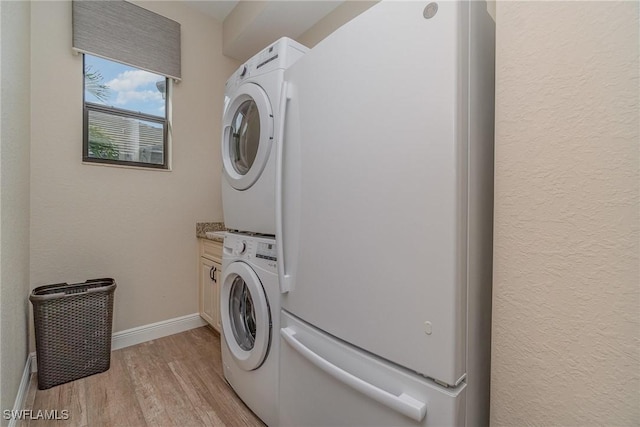 laundry room featuring baseboards, light wood-style flooring, stacked washer and clothes dryer, and cabinet space