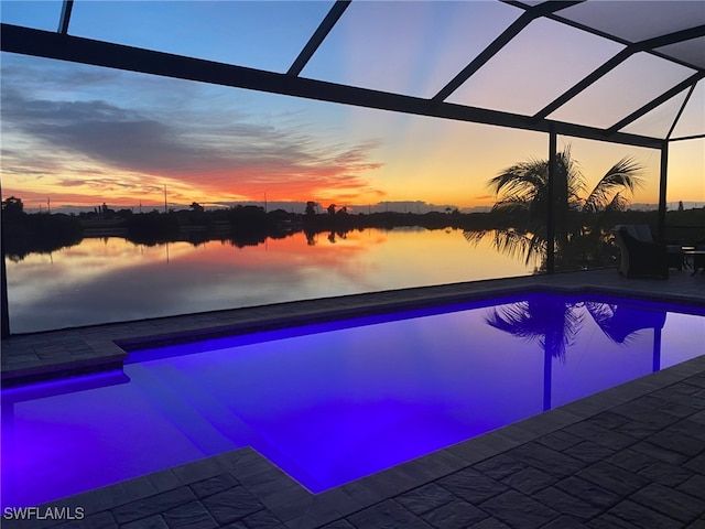 pool at dusk featuring an outdoor pool, a patio area, and a water view