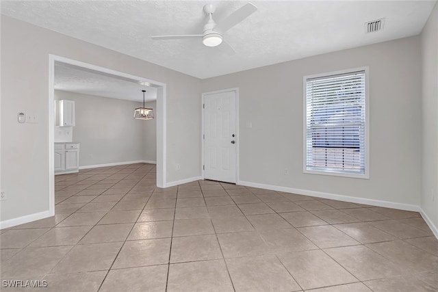 empty room featuring baseboards, visible vents, a ceiling fan, and light tile patterned flooring