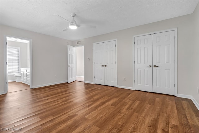 unfurnished bedroom featuring wood finished floors, a textured ceiling, baseboards, and two closets