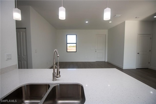 kitchen featuring dark wood-type flooring, light stone countertops, hanging light fixtures, and sink