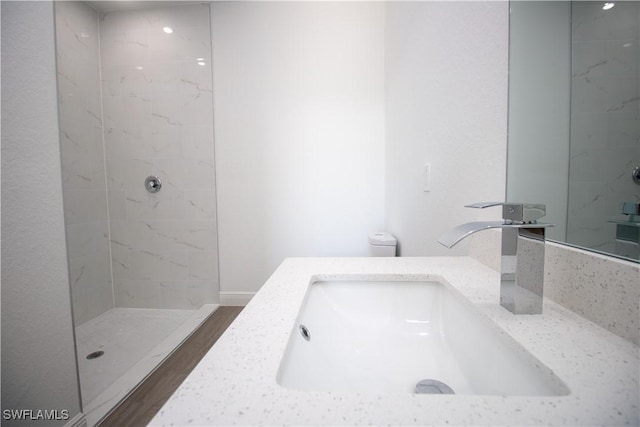 bathroom featuring hardwood / wood-style flooring, tiled shower, and vanity