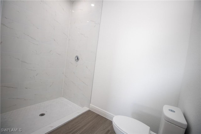 bathroom featuring wood-type flooring, toilet, and a tile shower