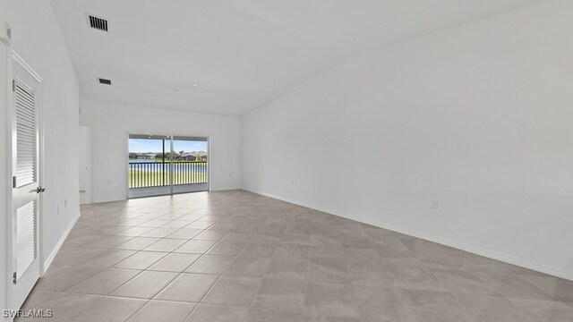 tiled spare room featuring vaulted ceiling and a water view