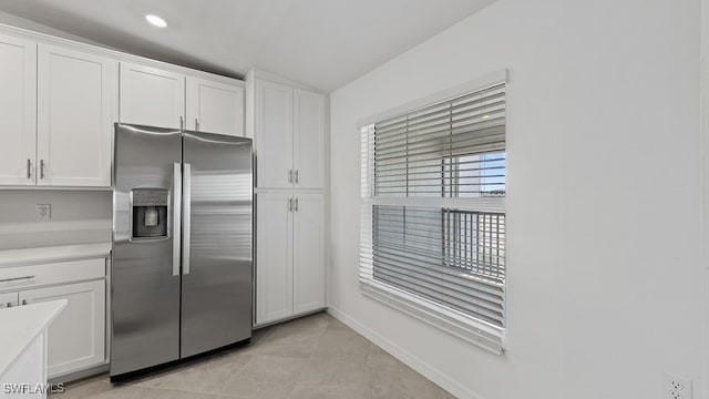 kitchen featuring light tile patterned floors, white cabinetry, stainless steel fridge, and vaulted ceiling