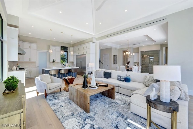 living room with a chandelier, light hardwood / wood-style floors, and a raised ceiling