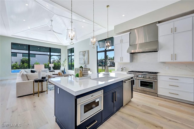 kitchen featuring sink, white cabinets, decorative light fixtures, a raised ceiling, and wall chimney exhaust hood