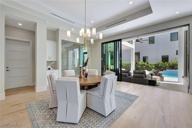 dining area with a raised ceiling, ceiling fan with notable chandelier, and light hardwood / wood-style flooring