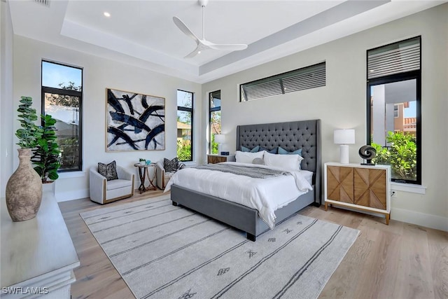 bedroom featuring multiple windows, light hardwood / wood-style flooring, and a tray ceiling