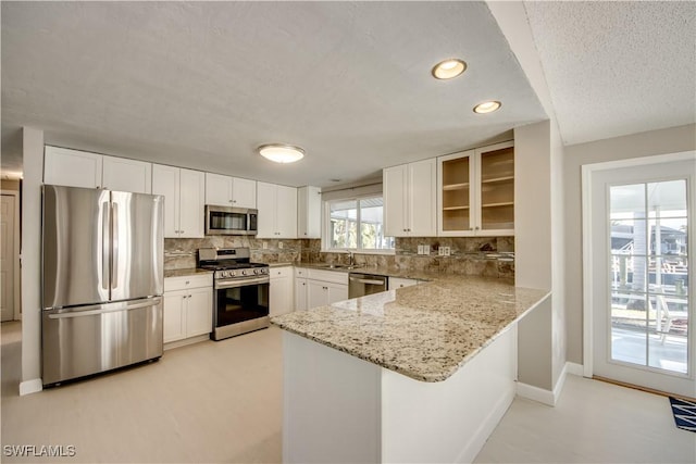 kitchen with stainless steel appliances, tasteful backsplash, light stone countertops, white cabinets, and kitchen peninsula