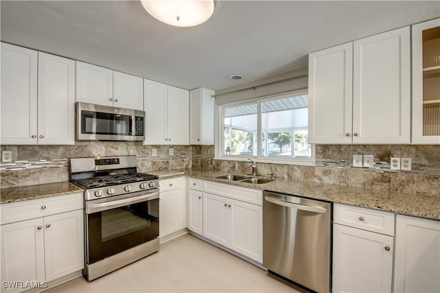 kitchen with sink, white cabinetry, backsplash, stainless steel appliances, and light stone countertops