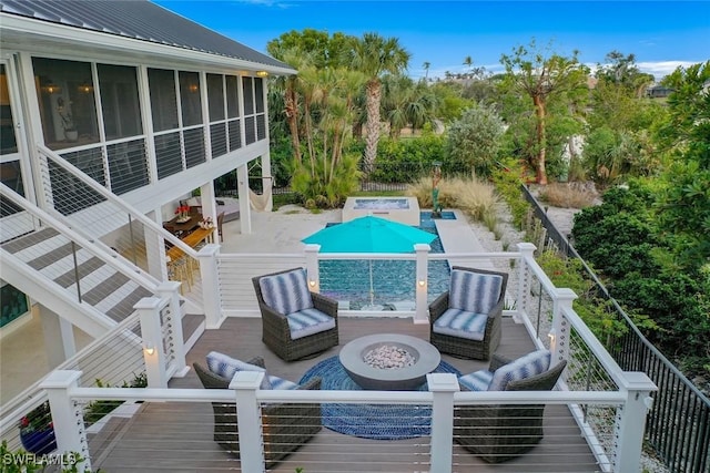 view of pool featuring a wooden deck, an outdoor fire pit, a sunroom, and a patio