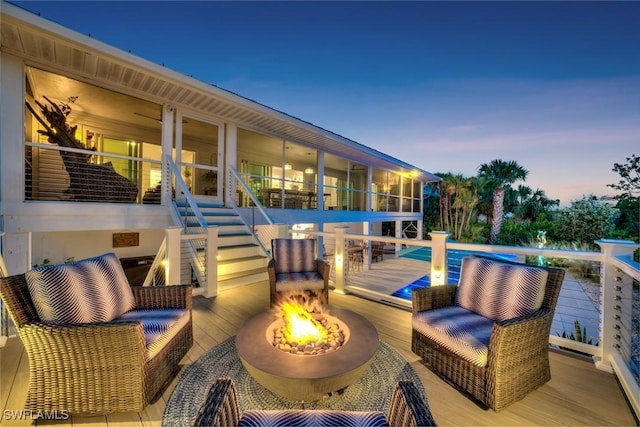 deck at dusk featuring a sunroom and an outdoor fire pit