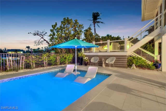 pool at dusk featuring a patio area and an outdoor bar