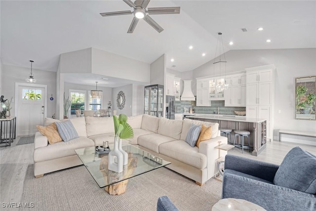 living room with lofted ceiling, ceiling fan with notable chandelier, and light hardwood / wood-style flooring