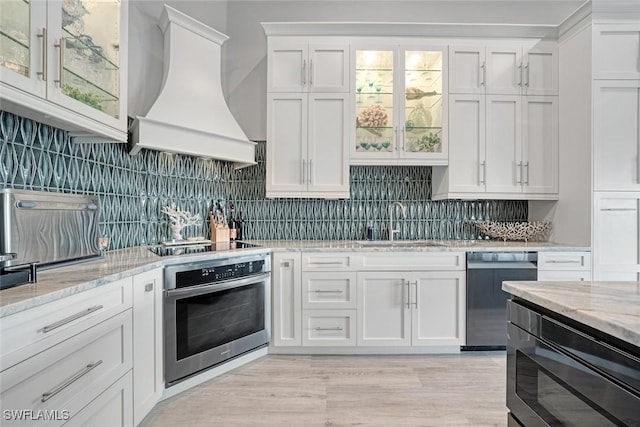 kitchen with black appliances, custom exhaust hood, decorative backsplash, light stone countertops, and white cabinets