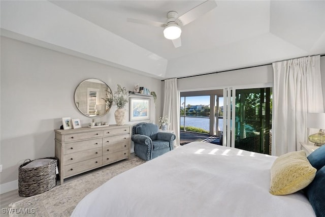 bedroom with ceiling fan, a tray ceiling, access to outside, and a water view