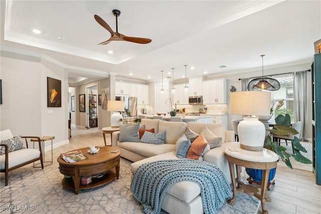 living room featuring ceiling fan, ornamental molding, light hardwood / wood-style flooring, and a tray ceiling